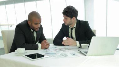 Birinde sakal ve diğerinde koyu renk saç olan iki kendine güvenen işadamı, gösterişli bir masa üzerindeki önemli belgeleri analiz ederek derin bir tartışmaya giriyorlar. Geniş pencereli modern ofis dekoru, doğal ışığın taşmasına izin veriyor.