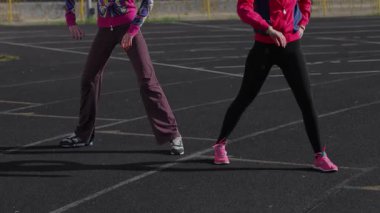 Canlı atletizm kıyafetleri giymiş iki genç kız, dinamik eğitim egzersizlerini güneşli bir pistte yapıyorlar, özverilerini ve enerjilerini sergiliyorlar. Sahne, gençlik kararlılığının özünü ve takım çalışmasının ruhunu yakalıyor.