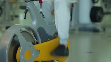 Orta Doğu kökenli odaklanmış genç bir adam hareketsiz bir bisiklete biniyor ve modern bir spor salonunda forma olan bağlılığını gösteriyor. Canlı atmosfer, şık spor aletleri ve parlak, motive edici bir çevreyle gelişir.