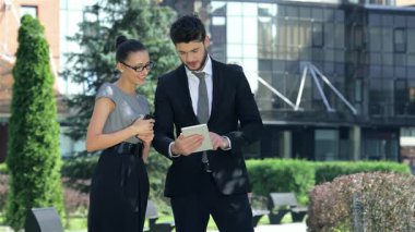 Kendine güvenen bir işadamı ve başarılı bir iş kadını, canlı bir ofis ortamında pozitif enerji saçan bir tablet üzerinde canlı bir işbirliğine girişirler. Şık kıyafetleri ve neşeli ifadeleri modern ve profesyonel bir ortaklığı yansıtıyor.