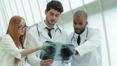 Parlak, çağdaş bir hastane ortamında, üç kendine güvenen doktor ve bir kadın sağlıklı akciğerlerin röntgenini dikkatle inceliyorlar. Odaklanmış ifadeleri ve profesyonel kıyafetleri hasta bakımına olan bağlılıklarını ve önemini vurguluyor.