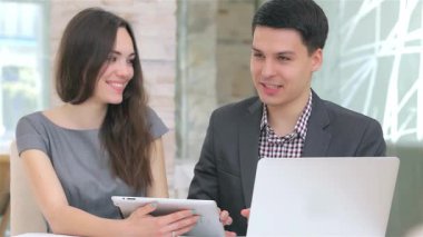 Genç, çekici bir iş adamı ve kadın şık bir tablet üzerindeki verileri analiz ederken, profesyonellik ve takım çalışması yayarak canlı bir tartışmaya girişirler. Arkadaşça gülümsemeleri ve odaklanmış ifadeleri davetkar bir atmosfer yaratıyor.