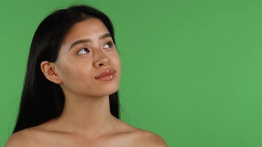Uzun, dalgalı saçları ve büyüleyici bir dudak halkası olan çarpıcı bir Asyalı kadın canlı yeşil bir krom arka planda rüya gibi yukarı bakıyor. Neşeli ifadesi pozitiflik ve güven saçıyor, izleyicileri mutlu anını paylaşmaya çağırıyor.