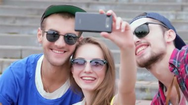 Mutluluk saçan üç genç arkadaş, neşeli bir selfie çekmek için güneşli basamaklarda toplanıyor, gülümsemeleri günü aydınlatıyor. Bu canlı sahne, arkadaşlığın ve kaygısız yaz titreşimlerinin özünü yakalıyor, şık güneş gözlüklerini ve neşeli gözlerini gösteriyor.
