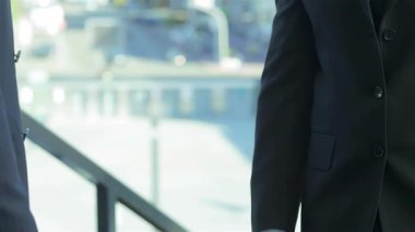 Keskin takım elbiseli iki profesyonel işadamı, başarılı bir ortaklığı simgeleyen sıkı bir tokalaşmaya giriyorlar. Parlak kentsel zemin, kurumsal başarının özünü gözler önüne sererek, hırs ve işbirliği atmosferini artırıyor.