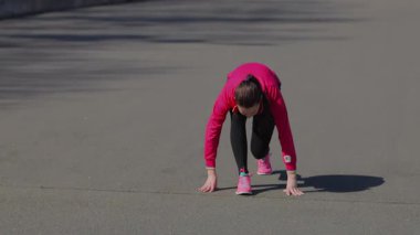 Odaklanmış genç bir kız hareketli bir stadyum pistinin başlangıç çizgisinde çömelmiş, harekete geçmeye hazır. Pembe elbisesi pürüzsüz gri yüzeyle çok güzel zıtlaşıyor. Rekabetin heyecanını ve atletizmin ruhunu yakalıyor.