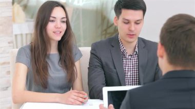 Genç ve çekici bir çift, modern bir ofiste gösterişli beyaz bir masada oturan iş projeleri hakkında dinamik bir tartışmaya girişiyor. Atmosfer, profesyonel ve gösterişli bir takım çalışmasına danışarak yaratıcılık ve hırsla doludur.