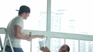 Parlak, havadar bir dairede, iki yetenekli işçi bir yenileme projesinde işbirliği yapıyor. Merdivene tünemiş bir adam, aşağıdaki takım arkadaşından neşeyle bir kova boya alıyor, takım çalışması ve uzay dönüşümüne olan bağlılığını gösteriyor.