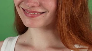 Kırpılmış bir stüdyo çekimi neşe saçan kızıl saçlı bir kadının göz kamaştırıcı gülüşünü canlı yeşil bir krom arka planda yakalar. Mükemmel, sağlıklı dişleri ışıl ışıl parlıyor, diş bakımının ve güzelliğin özünü somutlaştırıyor,