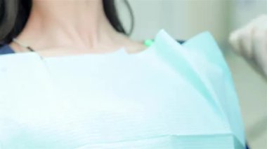 Genç bir kız, dişçi boynuna koruyucu bir peçete geçirir ve diş muayenesi için hazırlanır. Kliniğin parlak ve steril ortamı bakım ve profesyonellik duygusunu arttırır.