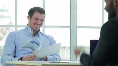 İki kendine güvenen iş adamı şık bir müzakere masasında canlı bir tartışmaya girişiyor, bir tanesi dizüstü bilgisayarla çalışırken bir iş sözleşmesini gözden geçiriyorlar. Sivri resmi giysiler içinde, ifadeleri başarı ve işbirliği yayarak bir atmosfer yaratıyor.