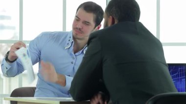 Kendine güvenen iki işadamı şık bir müzakere masasında dinamik bir tartışmaya girişerek, odaklanmış ifadelerle son bir raporu analiz ediyorlar. Sivri giysiler içinde profesyonellik ve takım çalışmasını somutlaştırıyorlar. Parlak bir ofis ortamıyla çevrelenmişler.