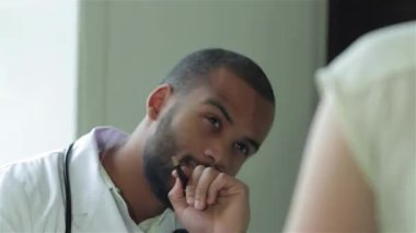 Odaklanmış bir doktor, modern bir klinikte şefkatli bir yaklaşım sergileyen hastasını dikkatle dinler. Boynunda bir steteskop ile, hastaları düşünceli bir şekilde düşünür, en iyi bakımı ve terziyi sağlamaya hazırdır.