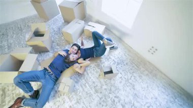 Konforlu, boş bir dairede, bir çift yerde uzanır, şefkatle kucaklaşır, paketlenmemiş kutularla çevrilidir. Neşeli ifadeleri yeni bir sayfa açmanın heyecanını yansıtıyor. Yeni, boş bir ev tuvalinde.