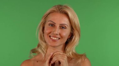 Büyüleyici bir stüdyo portresi. Çekici, olgun, dalgalı sarı saçlı bir kadın. Neşeli bir gülümsemeyle kameraya şşş yapıyor. Parmağı nazikçe dudaklarında duruyor, sırları davet ediyor ve bir flört ve cazibe atmosferi yaratıyor.