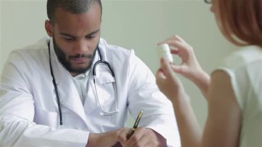 Parlak bir klinikte, steteskoplu odaklanmış bir doktor hastanın sağlık sorunlarını dikkatle dinlemektedir. Doktor özenle, destekleyici bir sağlık ortamında profesyonellik ve bakım içeren bir reçete yazar.