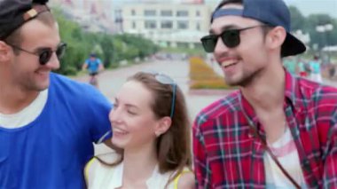 Üç genç arkadaş neşeli bir caddede neşeli bir şekilde yürüyor, sıcak güneşin altında gülüşmeler ve kahkahalar atıyorlar. Kaygısız ruhları ve şık kıyafetleri arkadaşlığın ve yaz eğlencesinin özünü yansıtıyor.