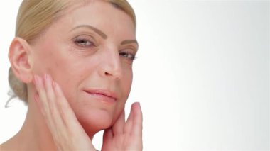 Zarif, orta yaşlı bir kadın yüzüne hafifçe dokunuyor, kusursuz cildini tertemiz beyaz bir arka plana vurguluyor. Bu büyüleyici portre güzellik ve güven yayıyor, özgüvenin ve zamansız zarafetin özünü sergiliyor.