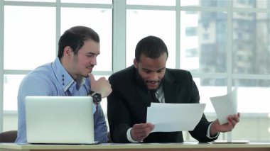 Zarif, modern bir ofiste, iki kendine güvenen işadamı iş sözleşmeleri üzerinde canlı bir tartışma içine girerken, biri belgeleri dikkatle incelerken diğeri de gözlemliyor. Resmi kıyafetleri ve odaklı ifadeleri profesyonelliği vurguluyor.