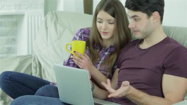 Neşeli bir çift kanepede rahat bir anın tadını çıkarır. Bir dizüstü bilgisayarla uğraşırken çaylarını yudumlar ve gülümsemelerini paylaşırlar. Neşeli şakaları ve rahat atmosferleri, canlı bir arkadaşlık ve neşe sahnesi yaratıyor.