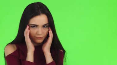 Uzun siyah saçlı çarpıcı bir genç kadın, canlı yeşil bir arka planda şakaklarını ovalarken gözle görülür şekilde stresli bir şekilde bir stüdyo ortamında yakalanır. Yüzündeki ifade yorgunluk ve rahatsızlığı gösteriyor. Aşırı çalışmanın bedelini yansıtıyor.