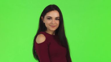 Uzun, dalgalı esmer saçlarıyla göz kamaştırıcı genç bir kadın, neşeli bir şekilde kameraya canlı yeşil bir arkaplanı işaret ederken neşeyle parıldıyor. Bulaşıcı tebessümü pozitif ve kendine güvenen bir gülümseme yayıyor, izleyicileri ona canlı bağlanmaya çağırıyor.