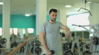 Ortadoğu kökenli kararlı bir genç adam triseps egzersizi yapıyor, parlak bir spor salonunda dambılları titizlikle kaldırıyor. Güçlü fiziği ve odaklanmış ifadesi fitness ve güç eğitimine olan bağlılığını vurguluyor.