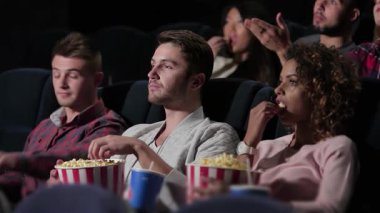 Canlı bir arkadaş grubu, samimi bir tiyatroda kahkaha ve duyguları paylaşan bir filme hayran kalıyor. Ellerinde patlamış mısır ve yanlarında içeceklerle, bu canlı sahne sinemanın neşesini ve ortak deneyimlerin büyüsünü yakalar.