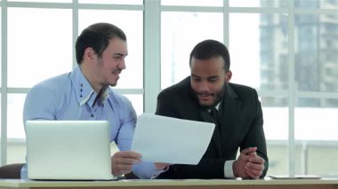 Gösterişli, güneşli bir ofiste, iki kendine güvenen işadamı, önemli belgeleri birlikte inceleyerek, dinamik bir tartışmaya girişirler. Resmi kıyafetleri ve odaklanmış ifadeleri profesyonel bir atmosferi, takım çalışmasını ve stratejik planlamayı yansıtıyor.