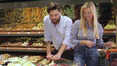 Tarz sahibi beyaz bir çift hareketli bir süpermarkette neşe içinde renkli dolmalık biber seçiyor. Neşeli sarışın kadın iki taze biber tutarken, yakışıklı sakallı partneri düşünceli bir şekilde tepsiye eğilip, canlı bir aşk sahnesi yaratıyor.