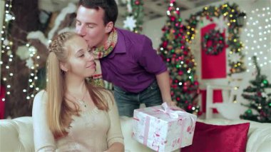 Sıcak kazaklar ve eşarplar giyen sevgi dolu bir çift, güzel dekore edilmiş bir Noel odasında hassas bir anı paylaşıyor. Genç adam kıvılcımlar saçan ışıklar ve bir şenlik ağacıyla çevrili güzel kızı öpmek için eğildi.