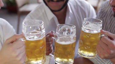 Canlı bir üst manzara, kutlama için soğuk bira bardaklarını birbirine tokuştururken üç neşeli genç adamı yakalıyor. Bu canlı sahne arkadaşlığı ve dostluğu simgeliyor, neşe dolu ifadelerini sergiliyorlar.