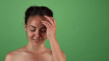 Çekici genç bir kadın canlı yeşil bir krom arka planda neşeli bir şekilde poz veriyor, büyüleyici gülüşü mutluluk saçıyor. Elleri nazikçe saçlarına dokunarak gençliğin coşkusunu ve kaygısız neşesini somutlaştırıyor. Seyircileri zevkine davet ediyor.