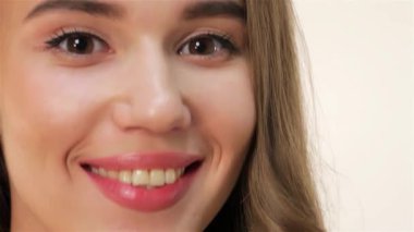 Bu çarpıcı yakın plan, parlak derisi ve canlı kırmızı dudaklarıyla mükemmel dişli bir gülümseme ile neşeli, genç beyaz bir kız yakalıyor. Yumuşak beyaz bir arkaplan, ışıl ışıl gözleri ve doğal güzellik pozitifliği ve sıcaklığı.