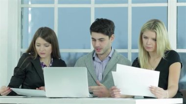 Genç profesyonellerden oluşan dinamik bir üçlü, bir erkek ve iki kadın, belgeler ve bir dizüstü bilgisayarı incelerken ortak bir tartışmaya girişirler. İfadeleri kararlılığı ve takım çalışmasını yansıtıyor, parlak, modern bir ofis zeminine karşı kurulmuş,