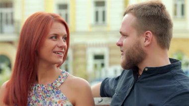 Birbirlerine sırılsıklam aşık büyüleyici bir çift, parkta bir bankta kucaklaşır, flörtöz bakışlar atar ve canlı bir şehir ortamında sıcak gülümsemeler takınırlar. Neşeli bağlantıları mutluluğu yayar. Romantizmin özünü şehrin canlı arka planında yakalar.