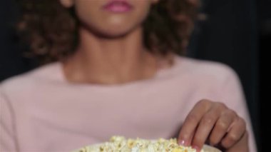 Kıvırcık saçlı güzel bir kız patlamış mısırın tadını çıkarıyor. Gözleri loş bir sinemada perdeye yapışık. Arkadaşlar ve çiftler kahkahalar ve abur cuburları paylaşarak keyifli bir sinematik deneyim yaratırken atmosfer heyecanla uğulduyor.