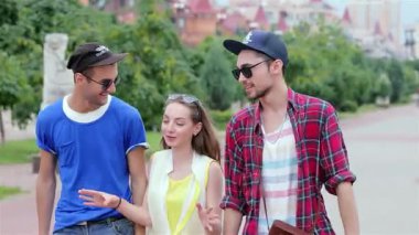 Üç genç arkadaş canlı bir caddede yürüyor, gülüyor ve sıcak güneşin altında hikayelerini paylaşıyorlar. Kaygısız gülüşleri ve neşeli jestleri, güzel bir günde arkadaşlığın özünü ve beraberliğin neşesini yakalar.