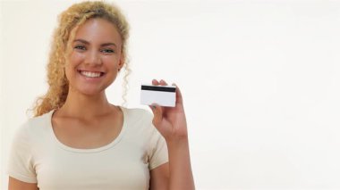 Bir elinde kredi kartı, diğer elinde de onay veren kıvırcık saçlı neşeli genç bir kadın. Parlak gülüşü güven ve başarı saçıyor. Temiz, beyaz bir arkaplan üzerine kurulu. Bu da enerjisini arttırıyor.