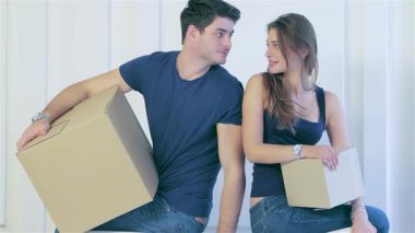 Neşeli bir çift, karton kutularla çevrili boş evlerinde duruyor. Yeni yolculuklarına başlarken heyecan saçıyorlar. Yüzlerindeki tebessümle, bir an için bir bağ kuruyorlar, taşınmanın sevincini somutlaştırıyorlar.