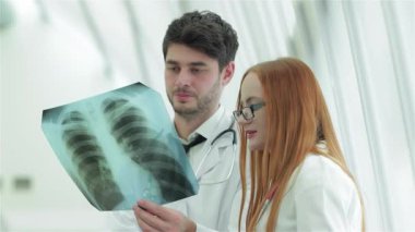 İki kendine güvenen doktor, bir erkek ve bir kadın, sigara içmenin tehlikelerini tartışmak için sağlıklı akciğerlerin röntgenini yakından inceliyorlar. Profesyonel kıyafetleri ve odaklanmış ifadeleri, sağlık sektöründe takım çalışmasının önemini vurgulayarak,