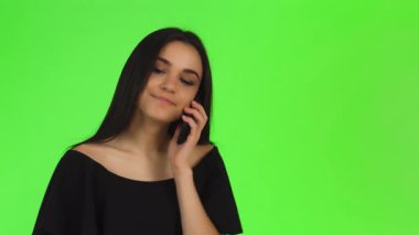 Parlak, koyu renk saçlı, şık, siyah, omuzsuz bir elbise giymiş genç bir kadın, canlı yeşil renkli bir arka plana karşı canlı bir telefon konuşması yaparken sevinçle ışıldıyor. Neşeli gülüşü ve kendinden emin tavırları...