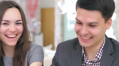 Genç ve çekici bir çiftin iş projeleri hakkında canlı bir tartışmaya girişmesi coşku ve takım çalışması yayıyor. Gülüşleri ve odaklanmış ifadeleri dinamik bir ortaklığı yansıtıyor, parlak, modern bir ofis zeminine karşı kurulmuş.