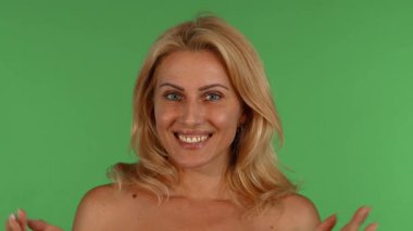 Çekici, olgun, dalgalı sarı saçlı bir kadın, canlı, yeşil renkli bir arka planda ellerini şakaya vurarak yüzünü kapatan bir duygu yelpazesi sergiliyor. Bu büyüleyici portre onun güzelliğini ve dışavurumunu vurguluyor.