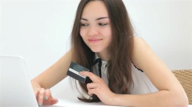 Uzun, dalgalı saçları olan genç bir kadın internetten alışveriş yaparken dizüstü bilgisayarına yakın kredi kartını tutuyor. Parlak, minimalist ortam alışveriş deneyiminin heyecanını arttırıyor, coşkusunu gösteriyor ve...