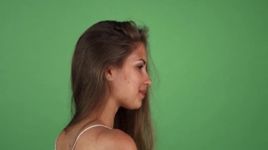 Parlak yeşil bir zemine karşı, uzun, dalgalı saçları ve güneşli bronzlaşmış ışıklarıyla sevinçle omzunun üzerinden geçen çarpıcı genç bir kadın. Kusursuz cildi ve neşeli ifadesi pozitif ve kendine güvenen seyircileri kucaklamaya davet ediyor.