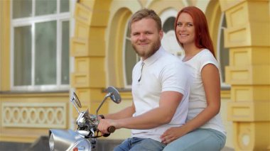 Sevimli genç bir çift, mutluluk saçan, güneşli bir caddede eski model bir scooter süren, kaygısız yaz titreşimlerini somutlaştıran. Gülümsemeleri ve rahat duruşları şehrin canlı mimarisi tarafından çevrelenmiş neşeli bir macerayı yansıtıyor.