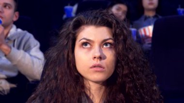 Kıvırcık saçlı çekici genç bir kadın, loş bir sinemada patlamış mısırın tadını çıkarırken filme hayran kalıyor. Onun odaklanmış ifadesi, lüks koltuklardaki izleyiciler tarafından çevrelenmiş film deneyiminin heyecanını yansıtıyor.