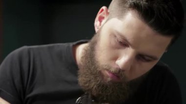 Dikkat çekici sakalı ve odaklanmış ifadesi olan usta bir berber şık bir berber dükkanında bir adamın saçını ve sakalını titizlikle kesiyor. Atmosfer canlı ve modern, tımar sanatını ve berber ile berber arasındaki bağı gösteriyor.