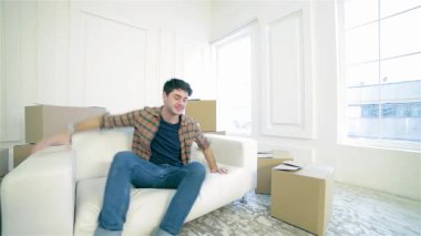 Neşeli bir çift parlak, boş bir dairede parlak beyaz bir kanepede oturuyor. Kutularla dolu, başparmaklarını kaldırırken mutluluk saçıyorlar. Etrafı çıplak duvarlar ve karton kaplarla çevrili gülümsemeleri yeni bir heyecanı yansıtıyor.